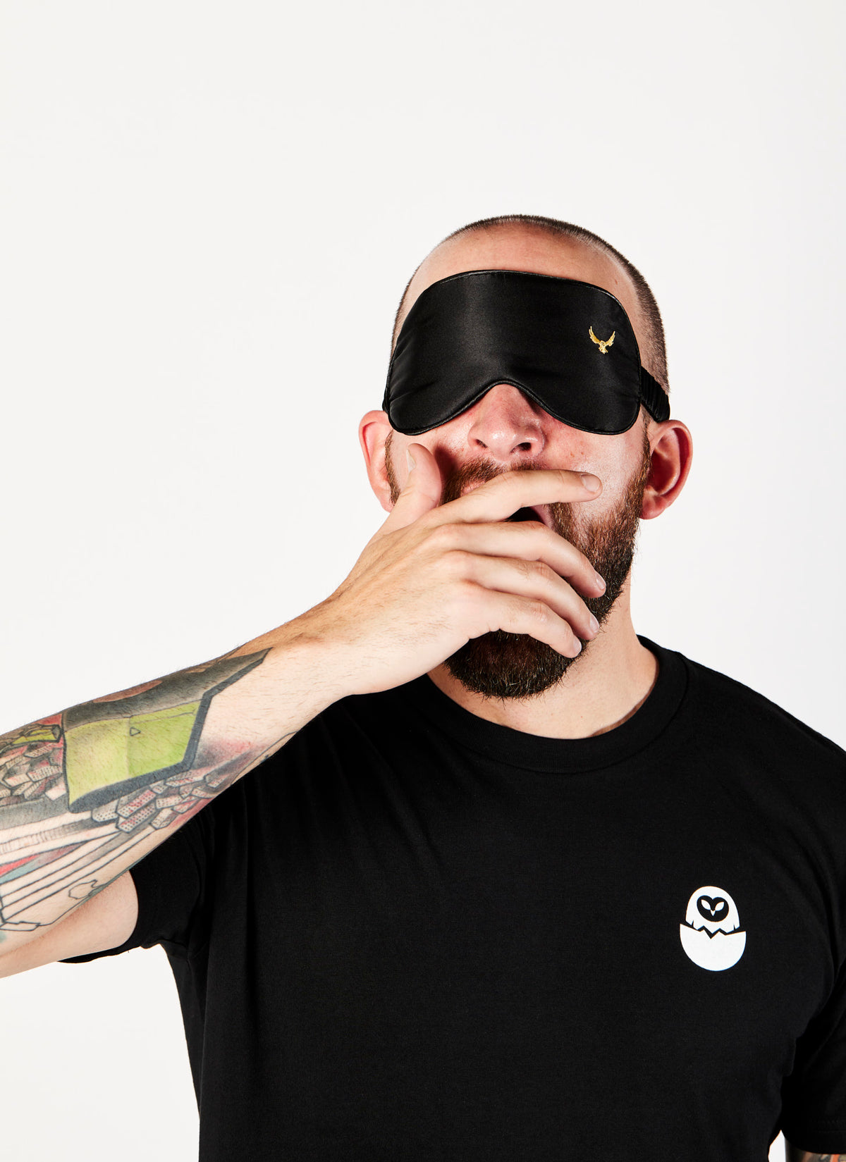 Front angle of a male video production crew member yawning while wearing a 100% silk black eye mask