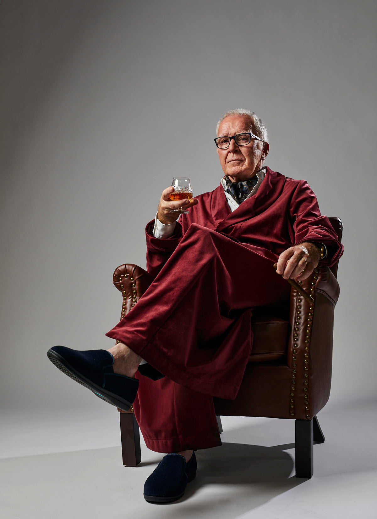 Low angle image of a wealthy man wearing a Red Video Production Robe holding a cigar and a glass of scotch