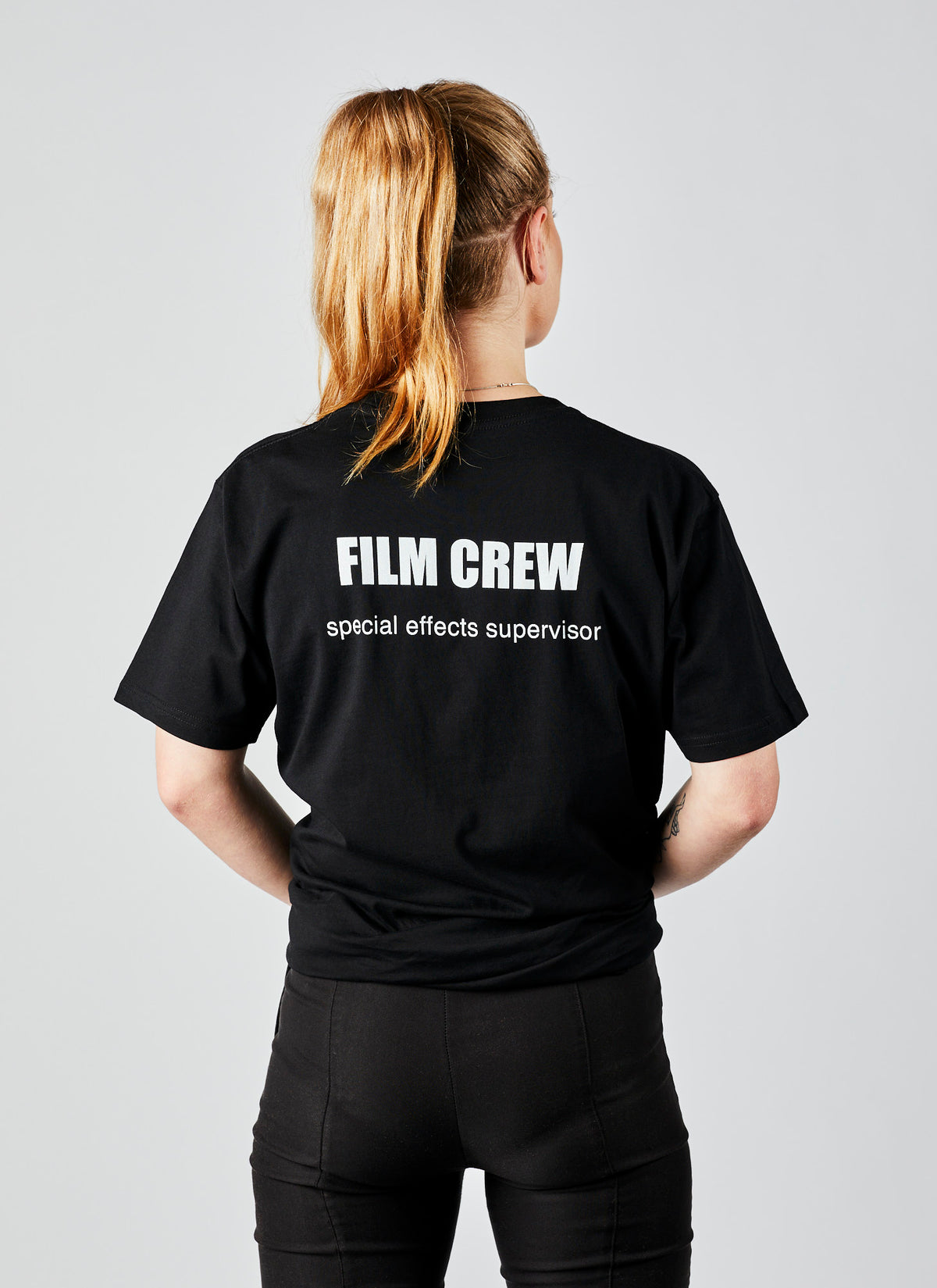 Reverse image of a woman wearing a black, short short sleeve shirt designed by Melbourne video production company, Enamoured Iris